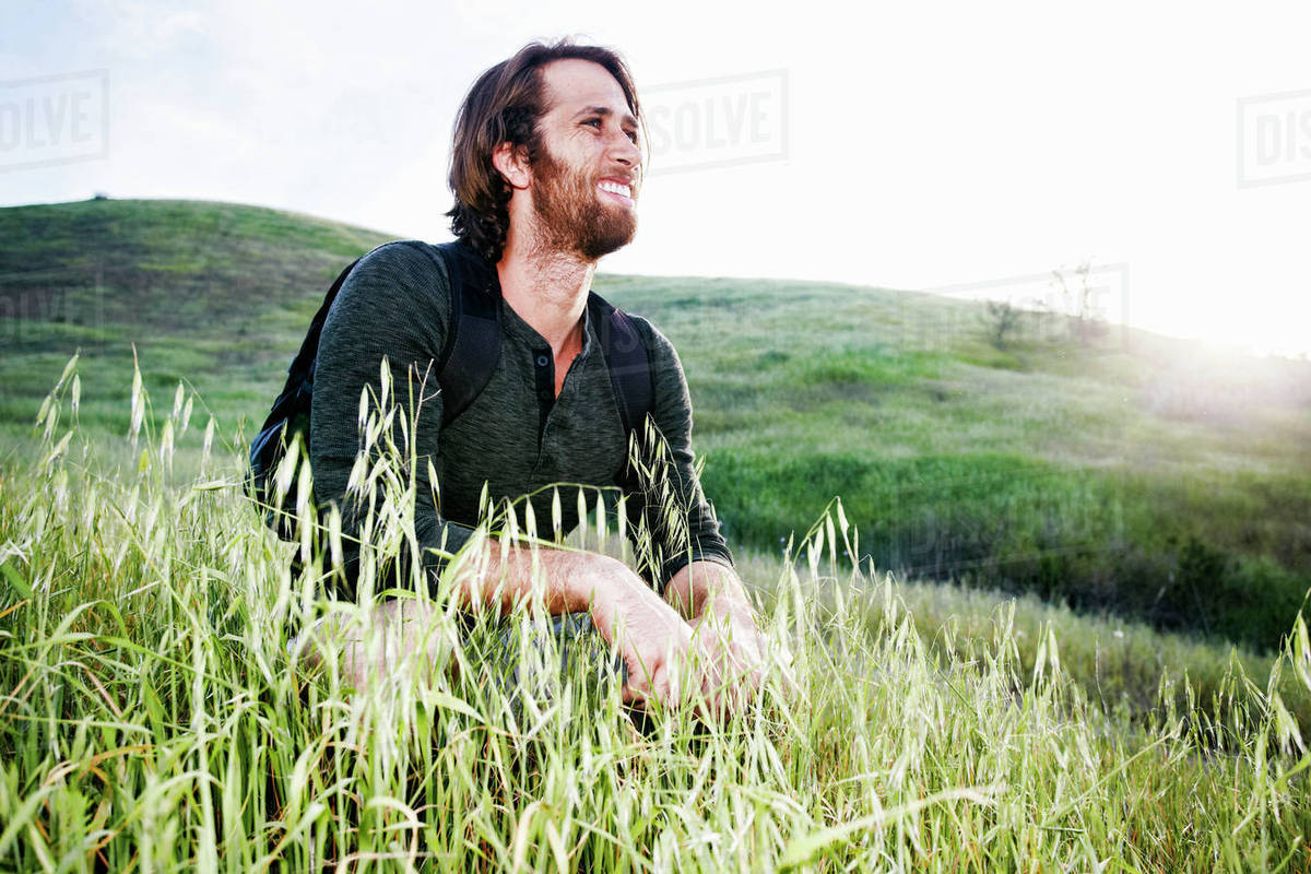 Caucasian hiker crouching in grass on mountain Stock Photo Dissolve