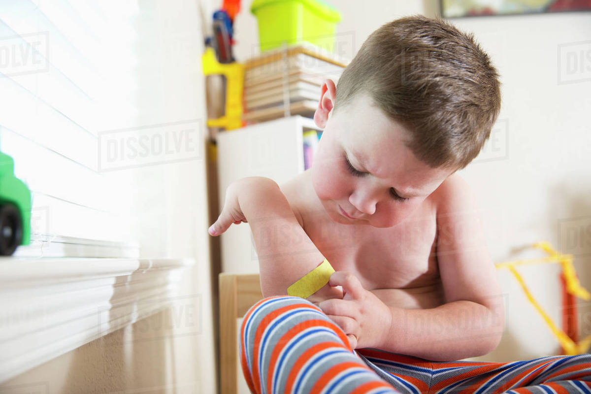Caucasian boy examining adhesive bandage on elbow Stock Photo Dissolve