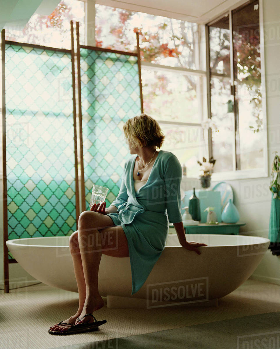 Woman sitting on edge of bathtub Stock Photo Dissolve
