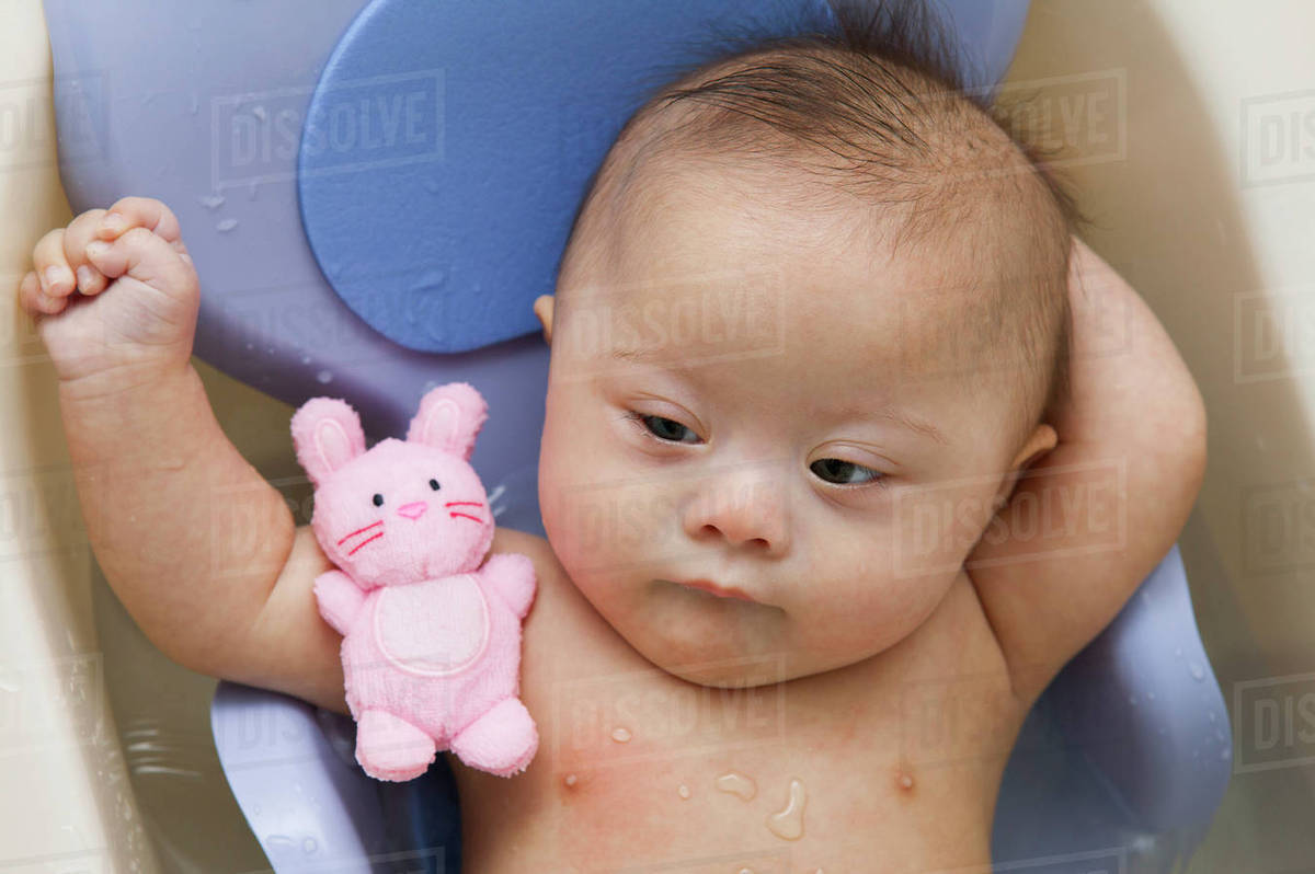 Mixed race Down Syndrome baby laying in plastic bathtub Stock Photo
