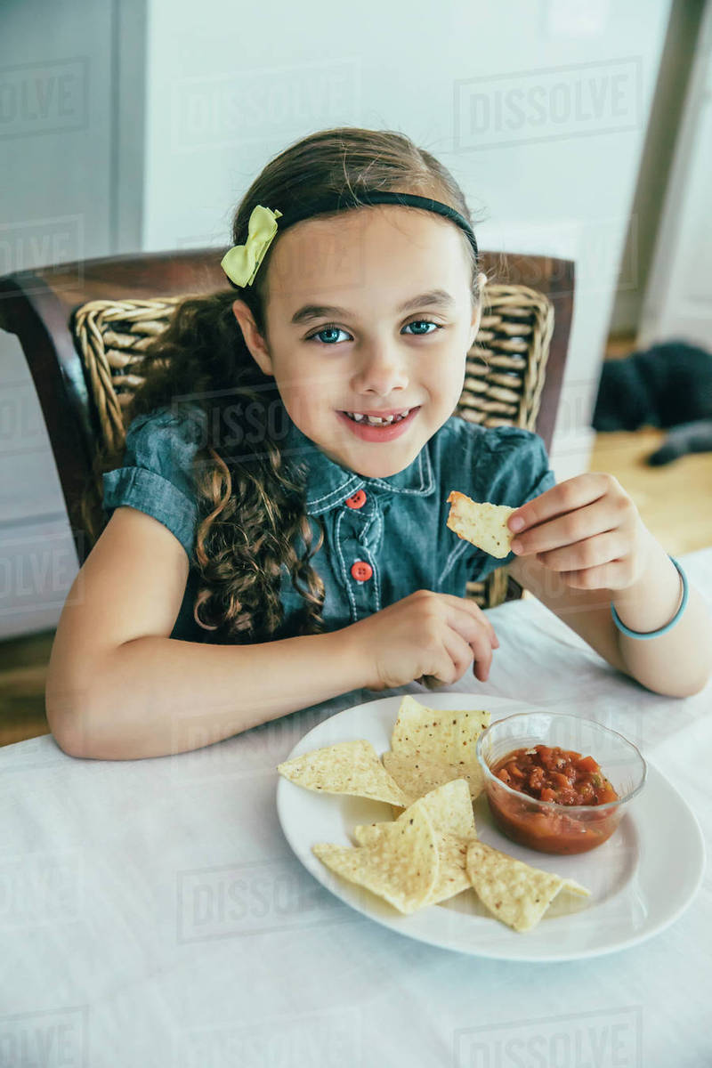 Mixed race girl eating chips and salsa at table Stock Photo Dissolve