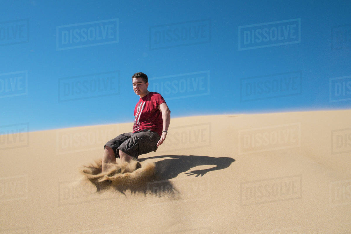 Caucasian teenage boy jumping on sand dune Stock Photo Dissolve
