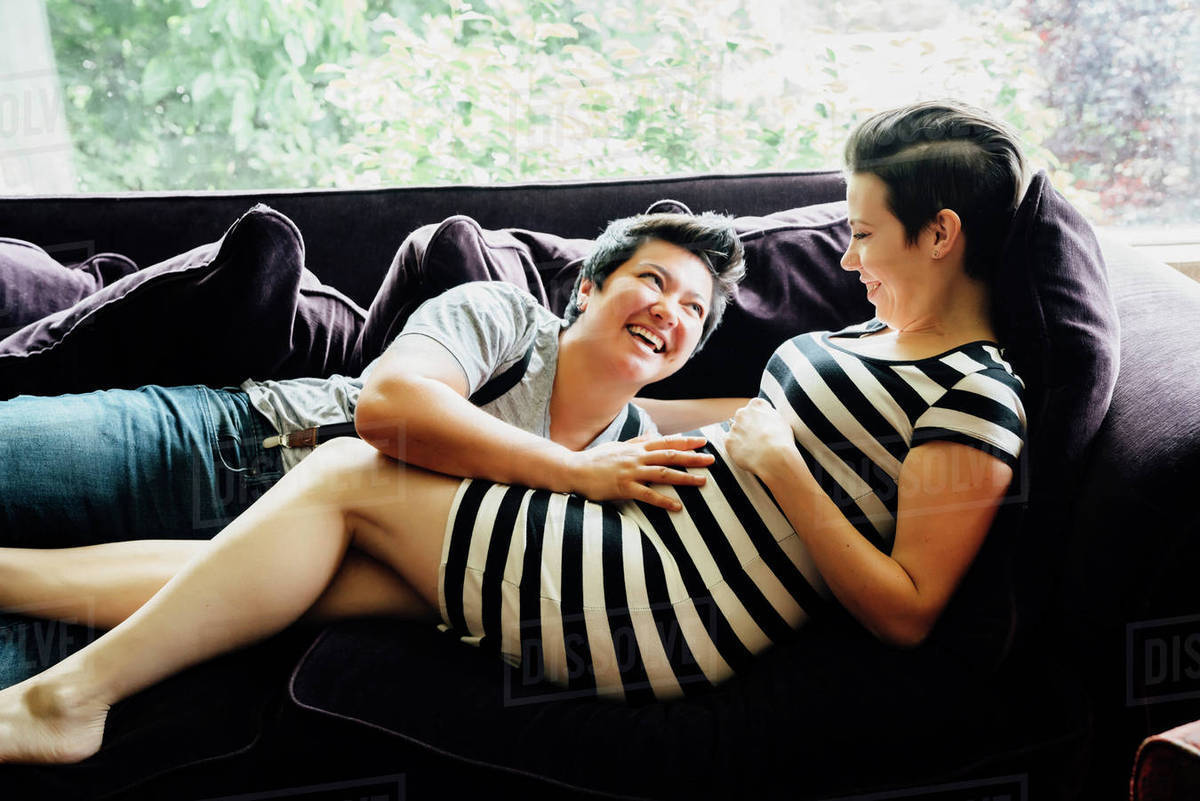 Pregnant lesbian couple cuddling on sofa Royalty-free stock photo