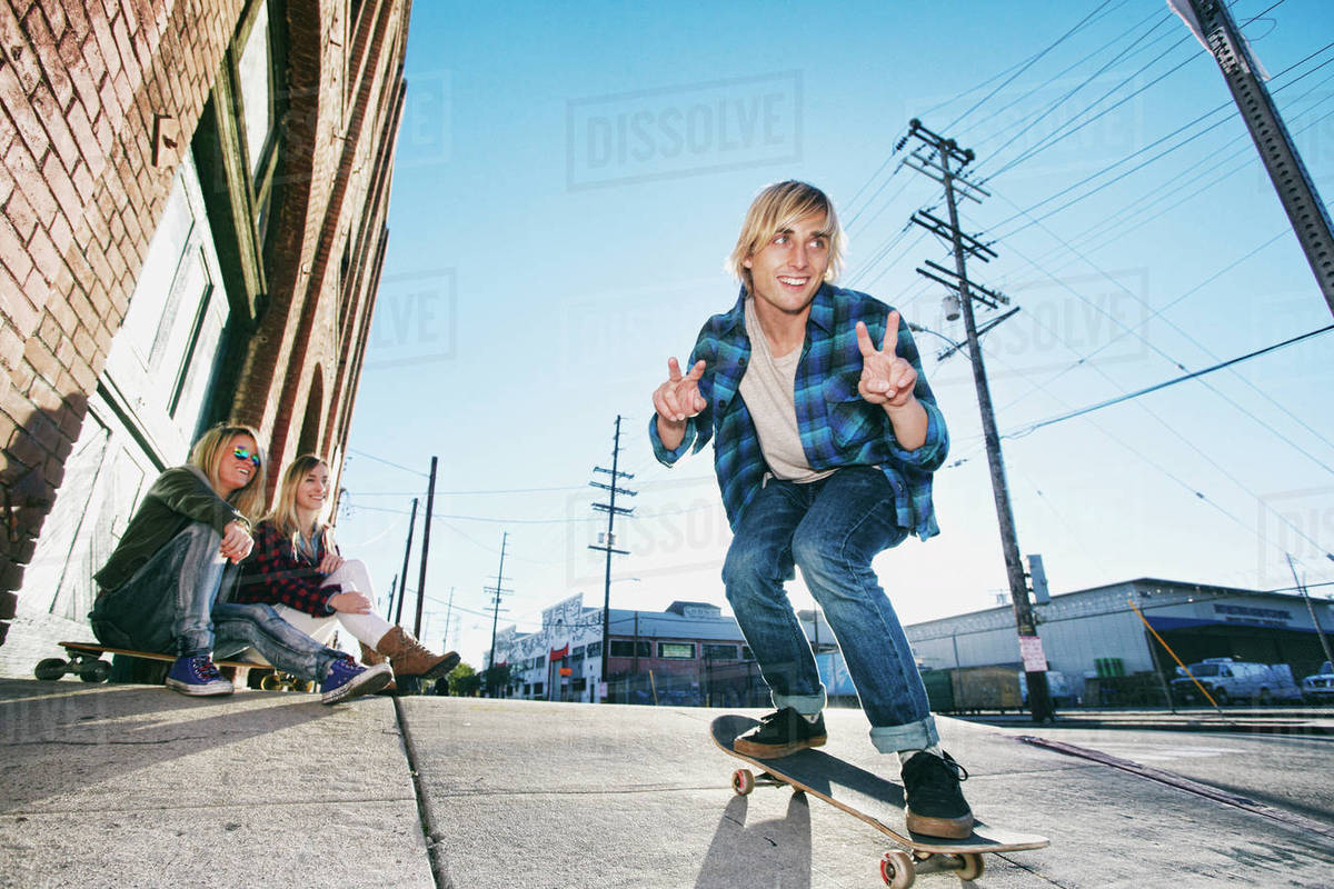 Women watching man skateboarding on urban sidewalk Stock Photo Dissolve