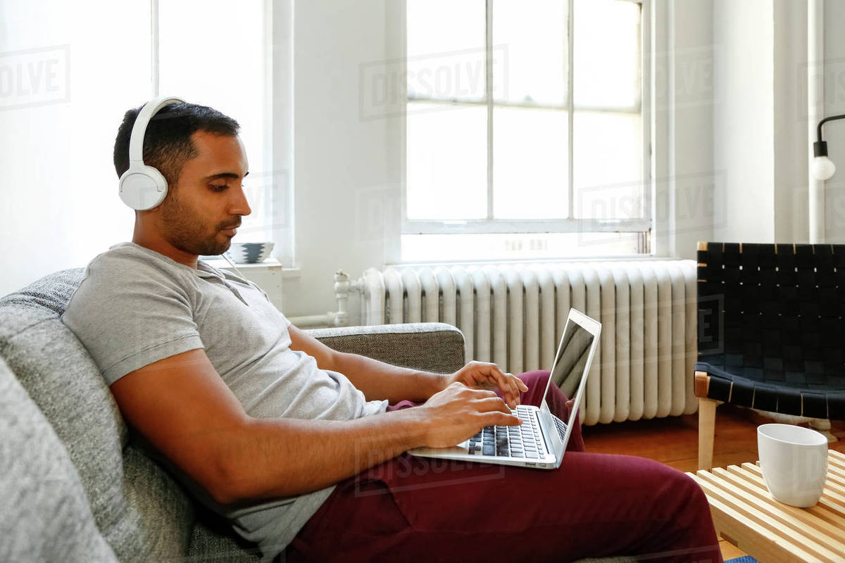 Mixed Race Man Sitting On Sofa Listening To Laptop With Headphones Stock Photo