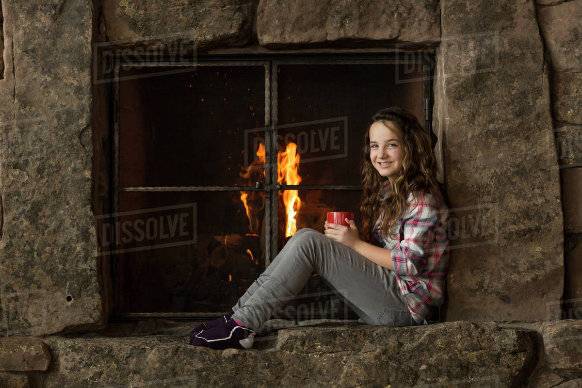 Smiling Caucasian girl sitting near fireplace Stock Photo Dissolve
