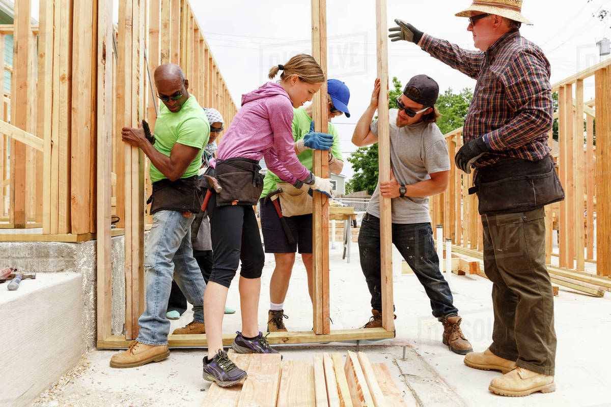 Volunteers lifting framed wall at construction site Stock Photo