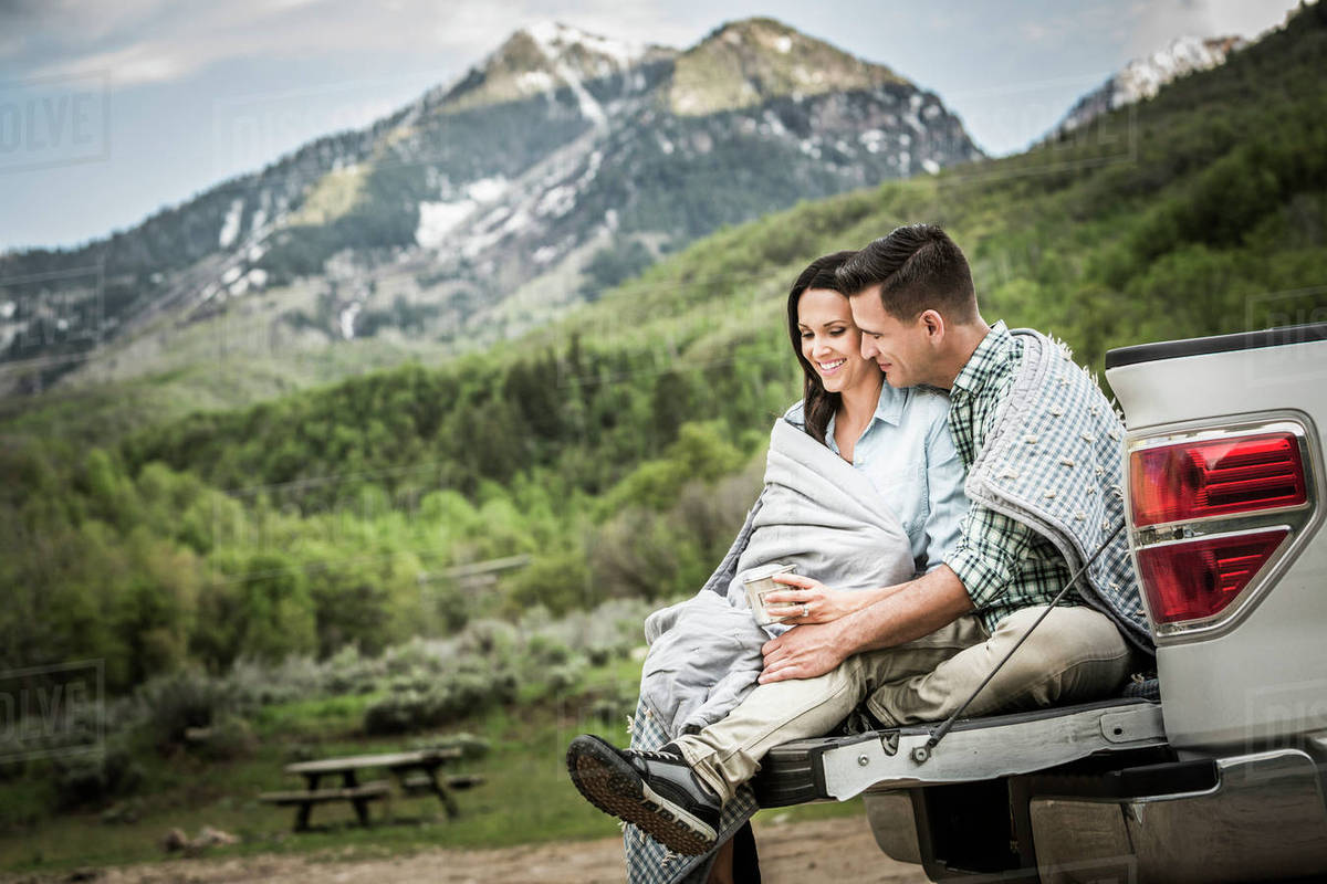 Couple wrapped in blanket sitting on bed of pickup truck Stock Photo