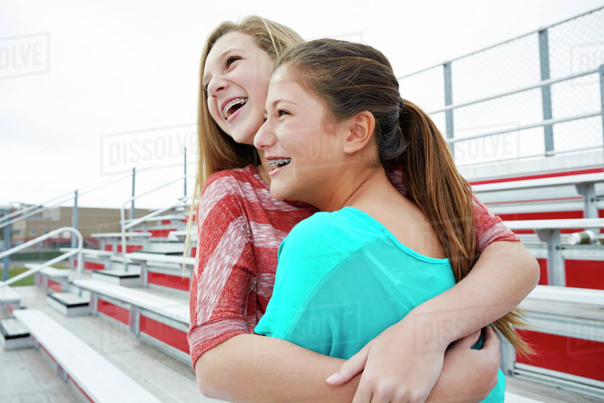 Teenage girls hugging on bleachers Stock Photo Dissolve