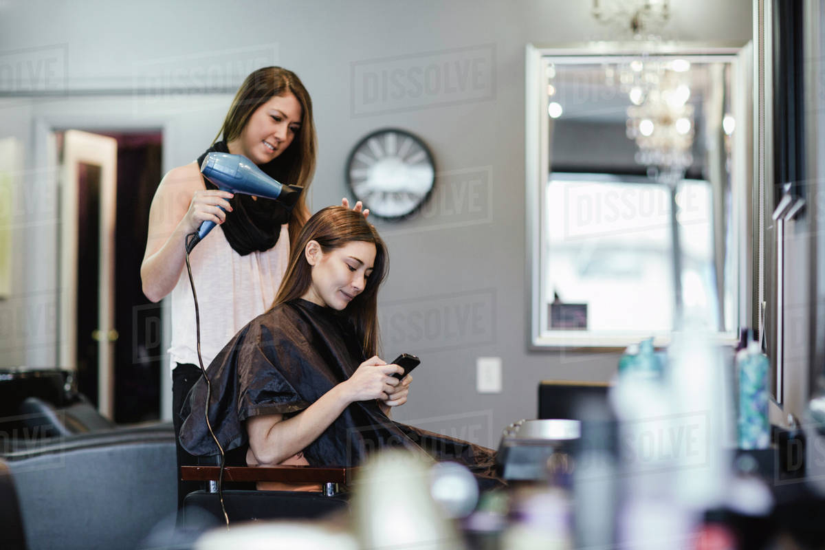 Stylist blow drying client's hair in salon Stock Photo Dissolve