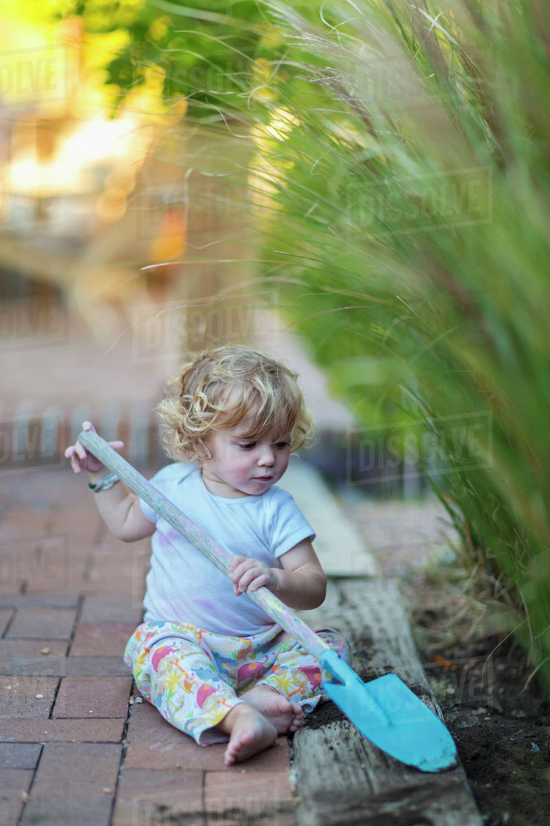 Caucasian boy playing with spade in garden Stock Photo Dissolve