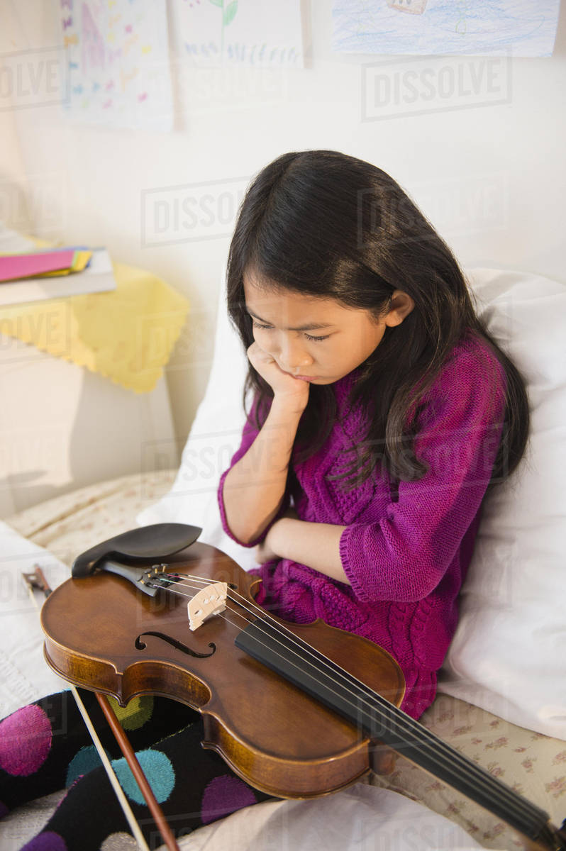 Pouting Vietnamese girl holding violin in bedroom Stock Photo Dissolve