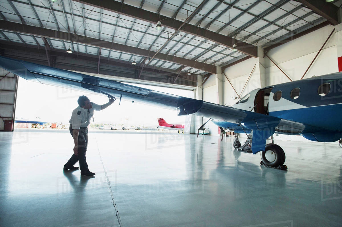 Caucasian pilot examining airplane in hangar Stock Photo Dissolve