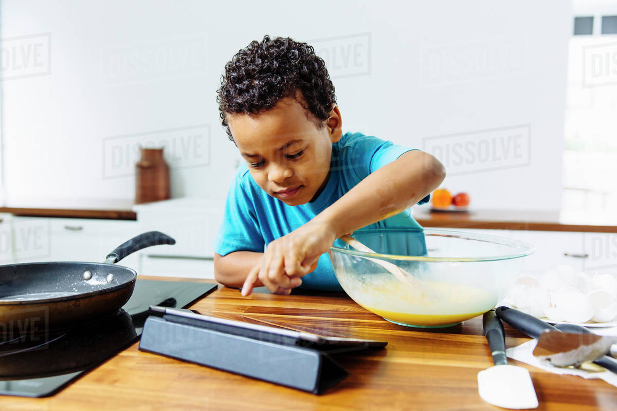 Mixed race boy cooking breakfast with digital tablet in kitchen Stock