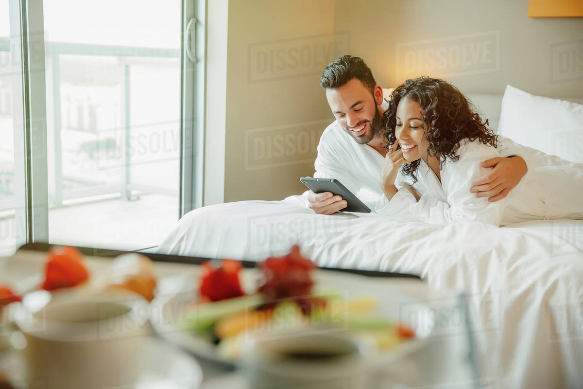 Couple using digital tablet on hotel bed Stock Photo Dissolve