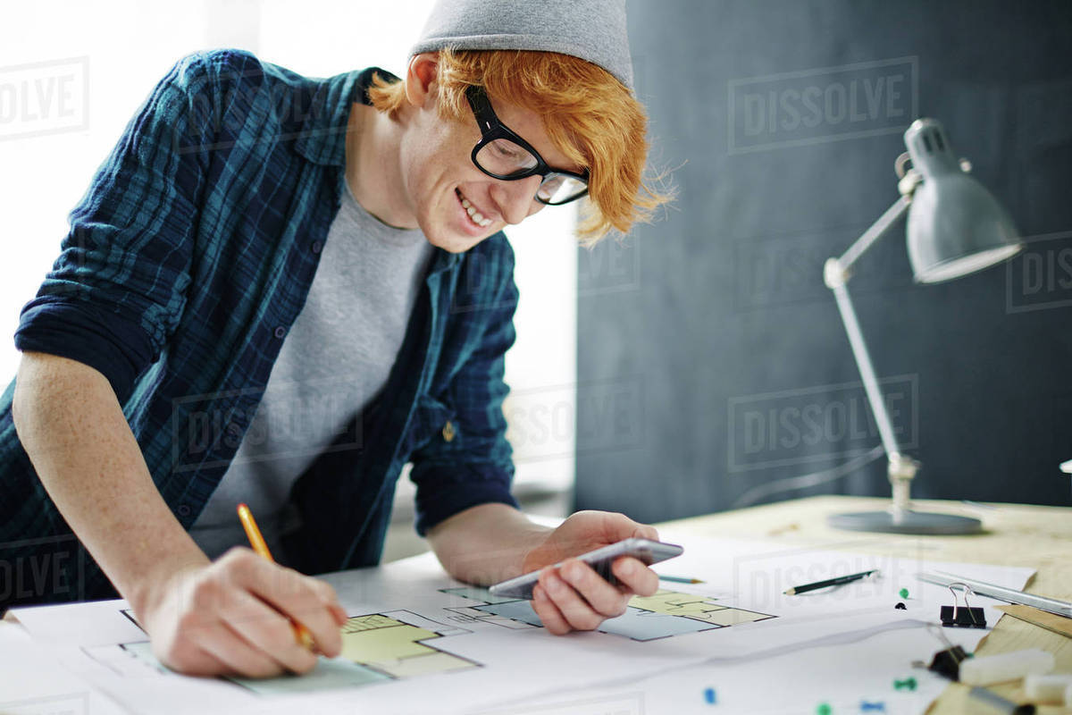 Young designer or architect using smartphone while drawing sketch Royalty-free stock photo