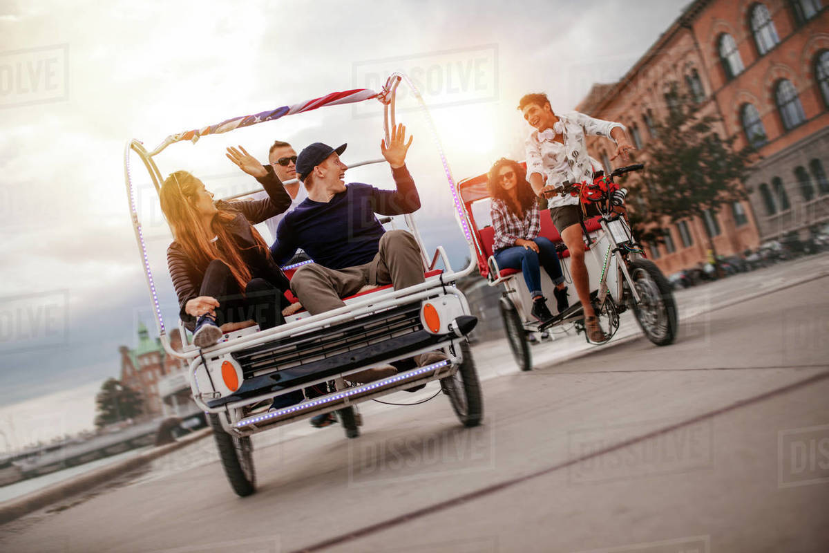 Group of friends having fun with two tricycles on road. Teenagers on