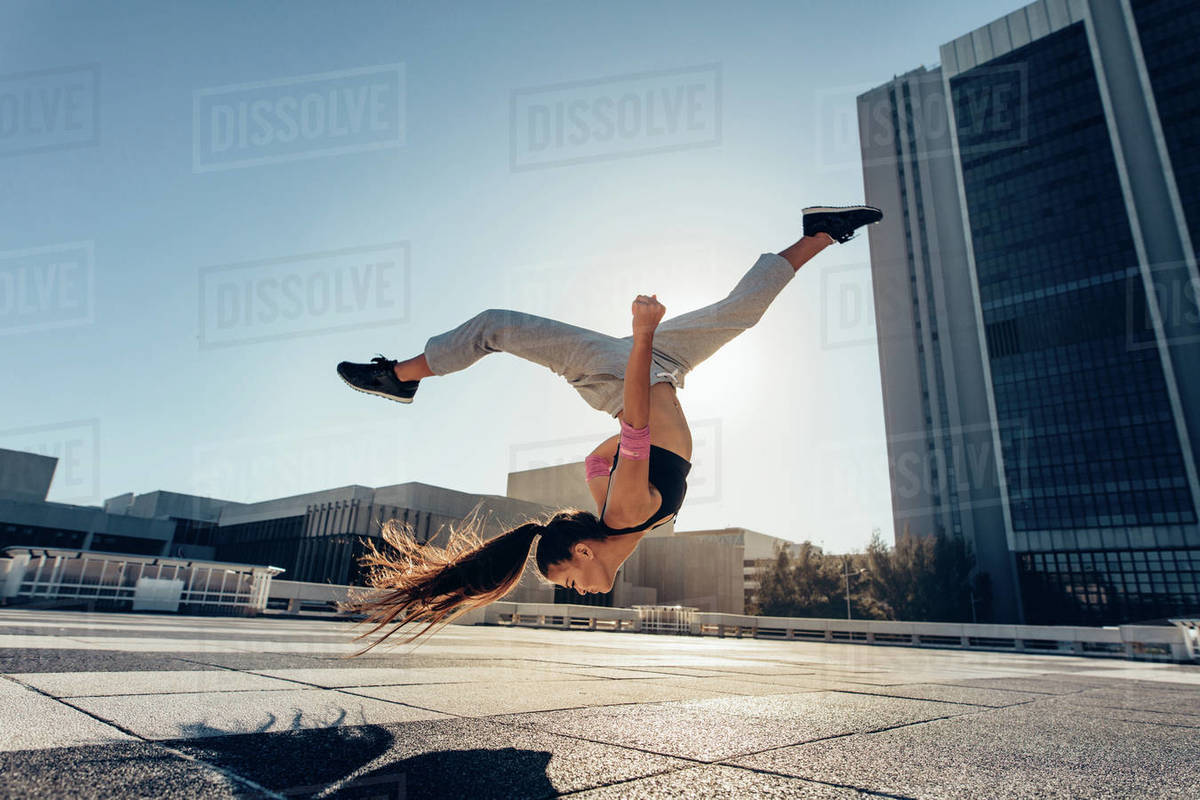 Young woman jumping high performing a frontflip outdoors in city. Female practicing tricking over urban city background. Royalty-free stock photo