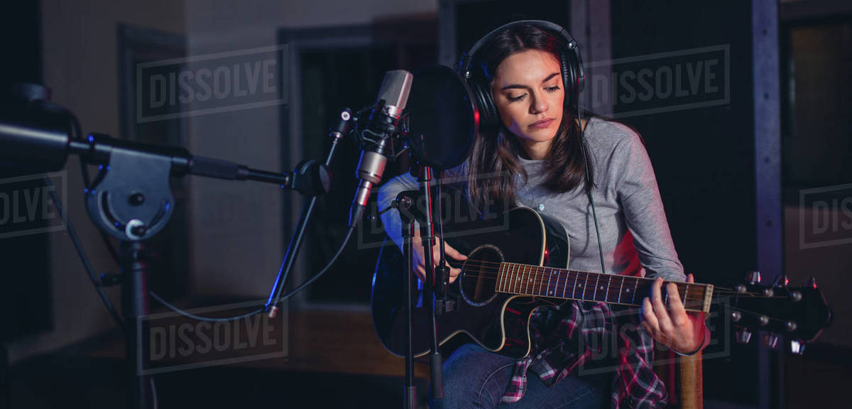 Female singer performing a song in studio and playing guitar. Woman ...
