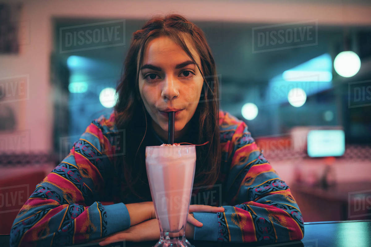 Woman drinking milkshake with straw at cafe. Female at cafe counter