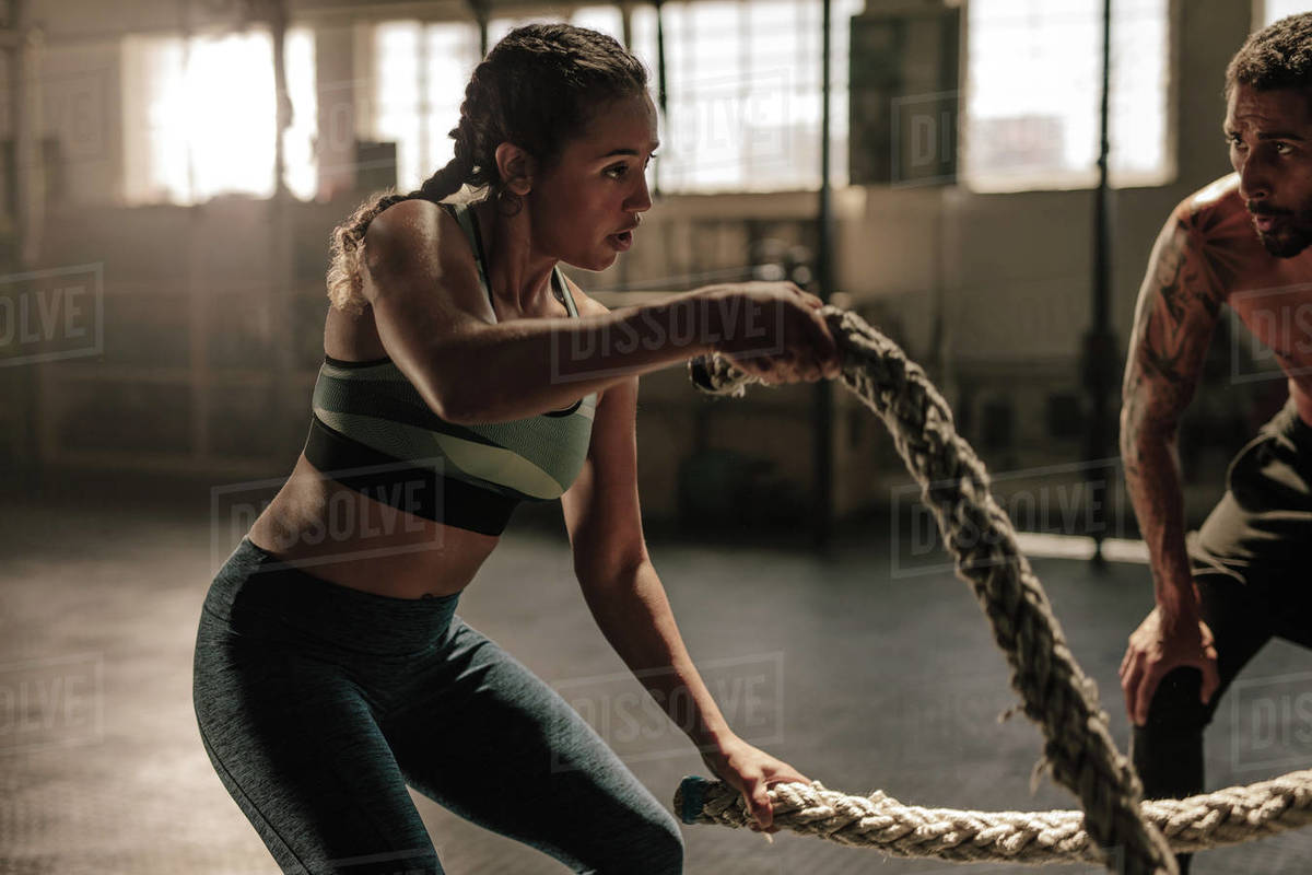 Female exercising with battle ropes at the gym with Athlete