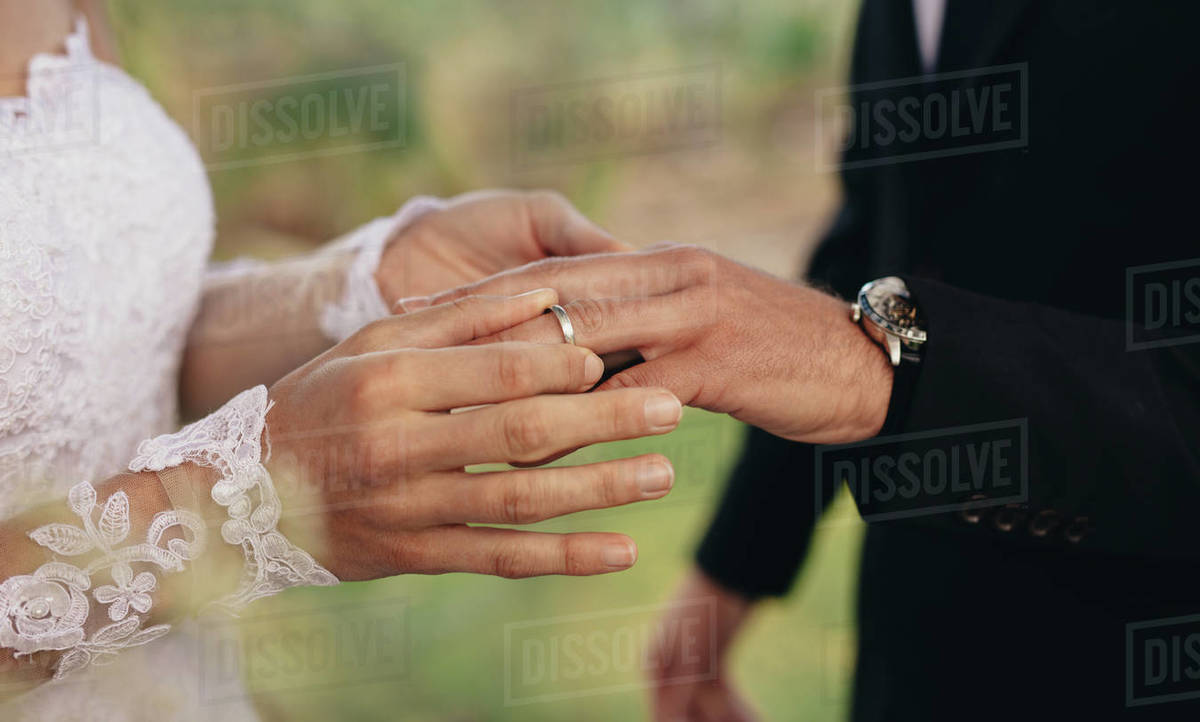 Closeup of bride putting a wedding ring onto the groom's finger