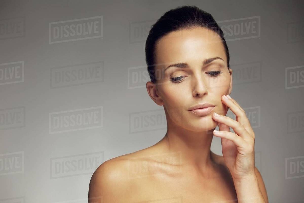 Close Up Portrait Of A Beautiful Young Brunette Holding Hand By Face Close Up Portrait Of A Beautiful Young Brunette Holding Hand By Face And Looking Down Attractive Woman With Skin Against Gray Background