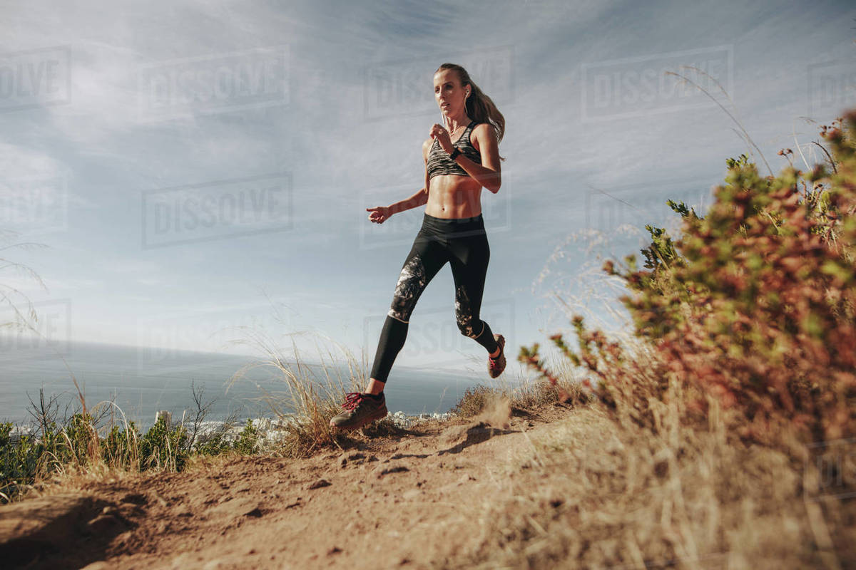 Fit sports woman sprinting over rocky trail on mountain. Woman running downhill on mountain path. Royalty-free stock photo