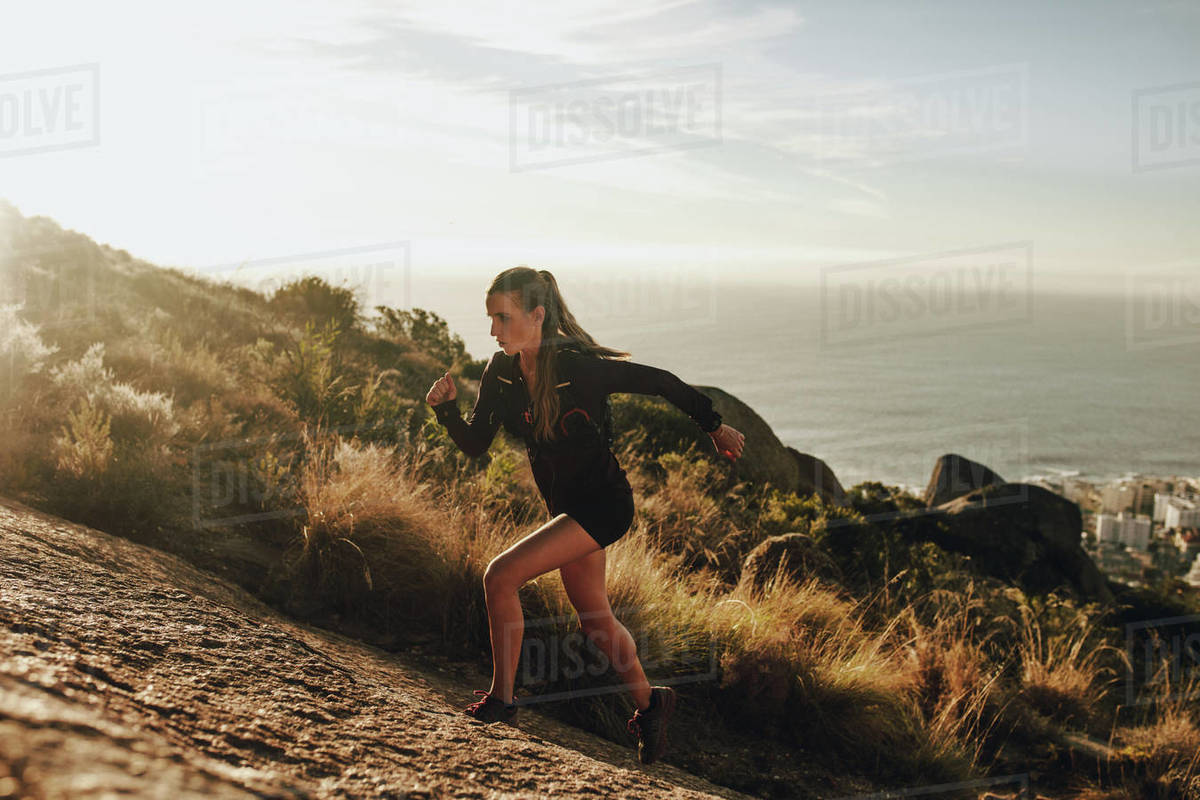 Fit young woman running up a rocky mountain Woman trail