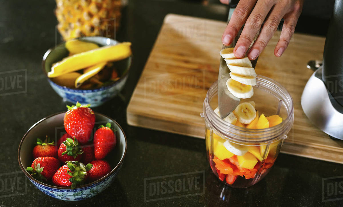 Hands of woman putting fruits in grinder bowl. Female making mix fruit