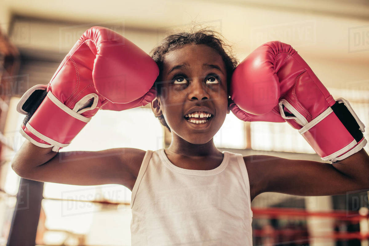 Kid wearing boxing gloves standing in a boxing ring touching her head
