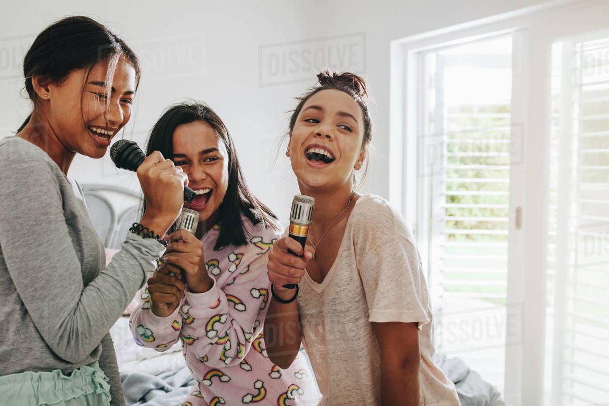 Teenage girls enjoying and having fun singing songs holding microphones
