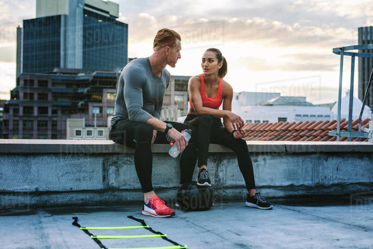Man and woman in fitness clothes relaxing on the rooftop during