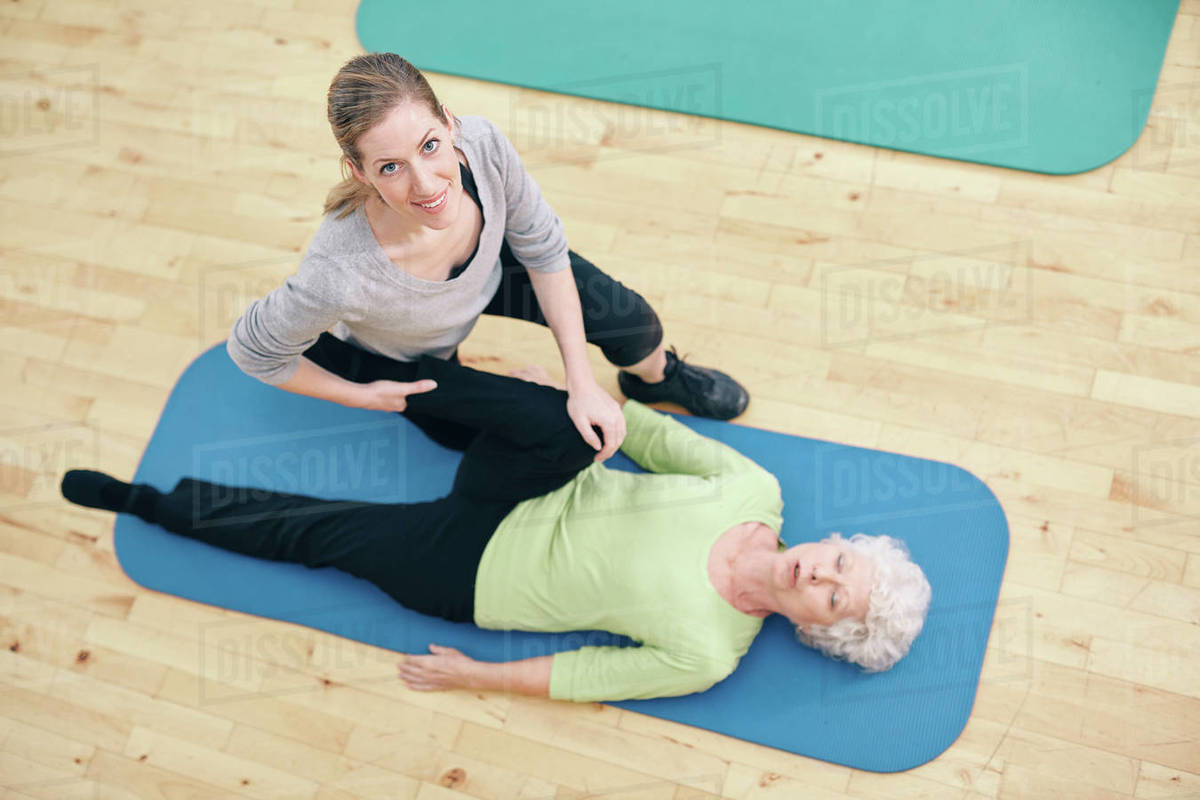 Top view of physical therapist helping senior woman do leg stretches at