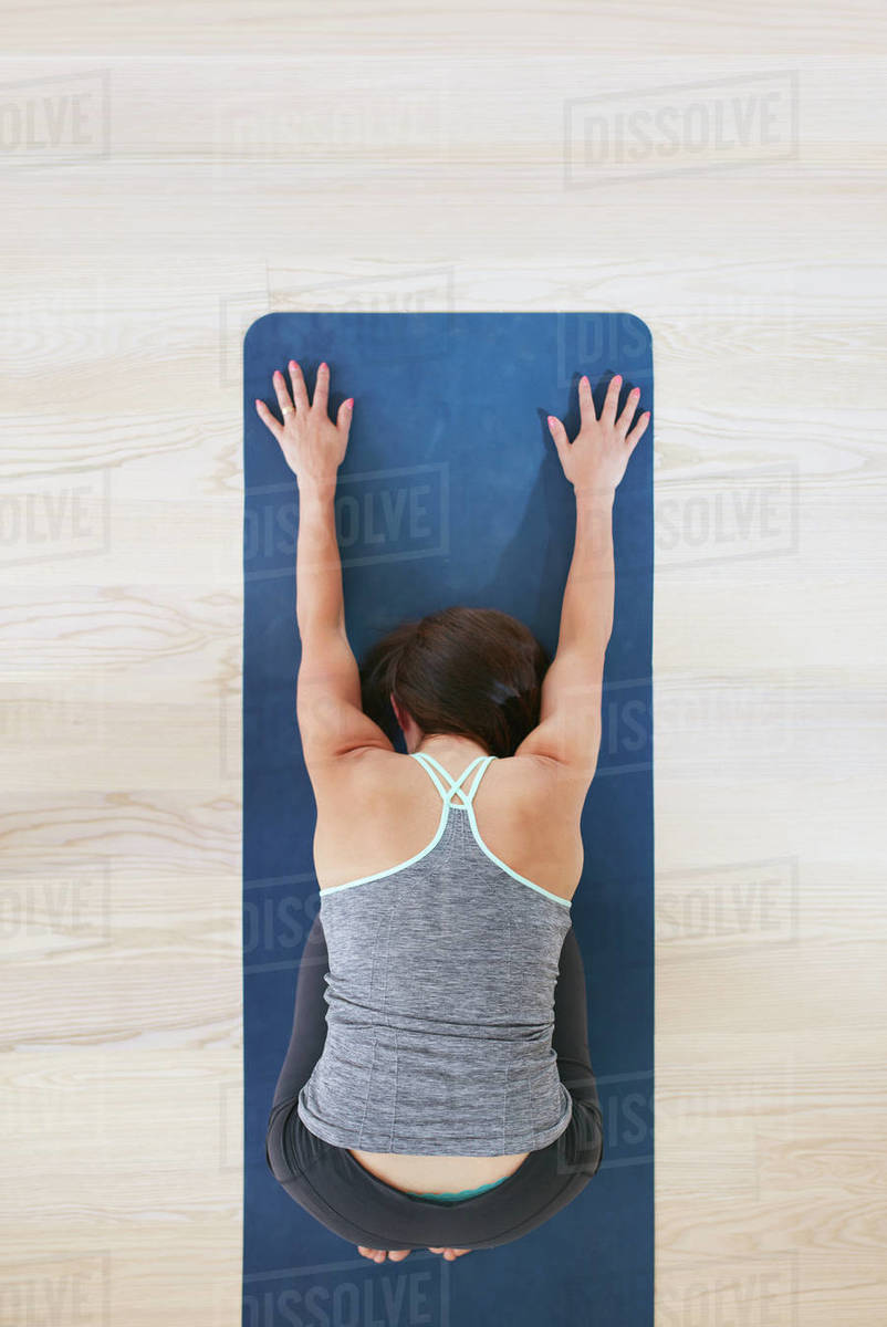 Top view of woman curls up and stretches forward, performing a yoga