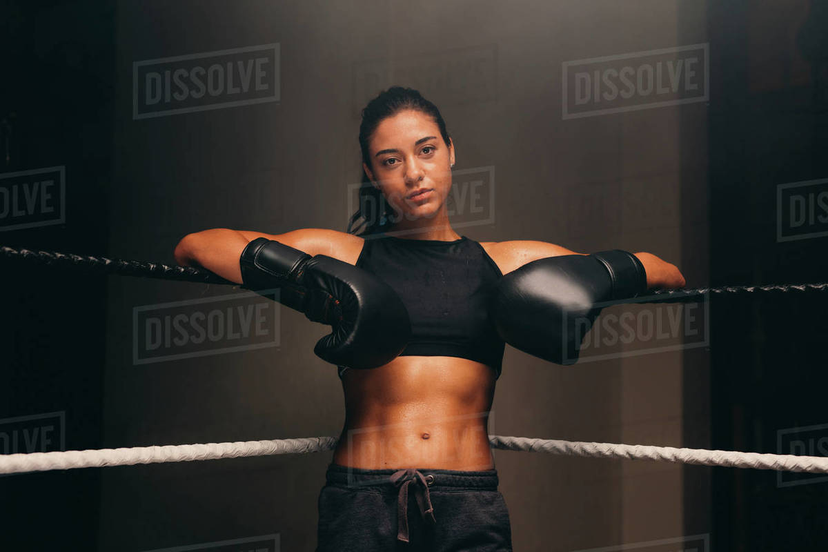 Serious beautiful fighter resting elbows on ropes of boxing ring with