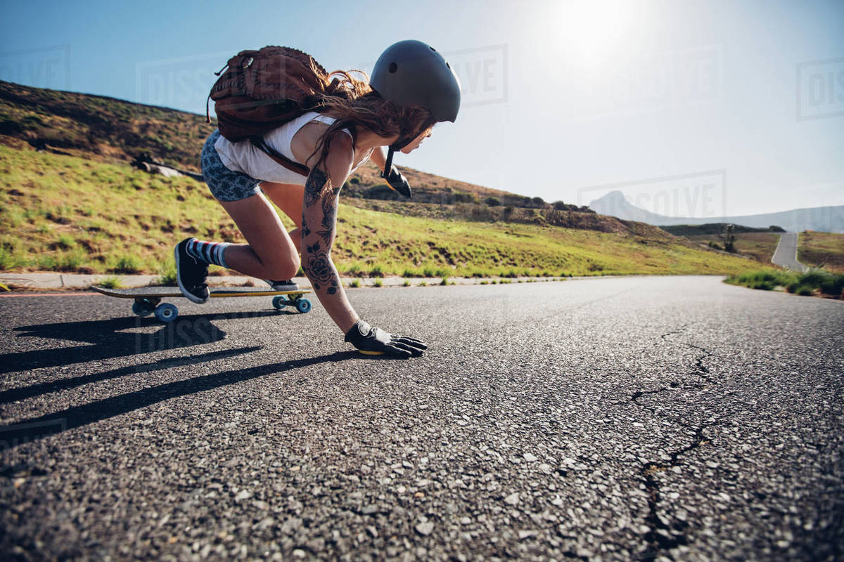 Young woman riding on her skateboard. Female skater practicing skating on country road. Royalty-free stock photo