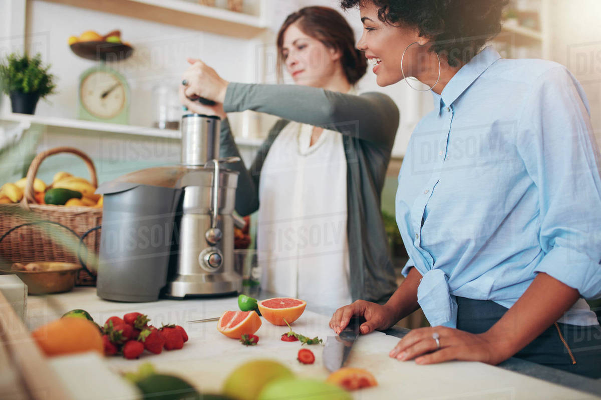 Women working at juice bar. Female putting fruits in juicer. Two young