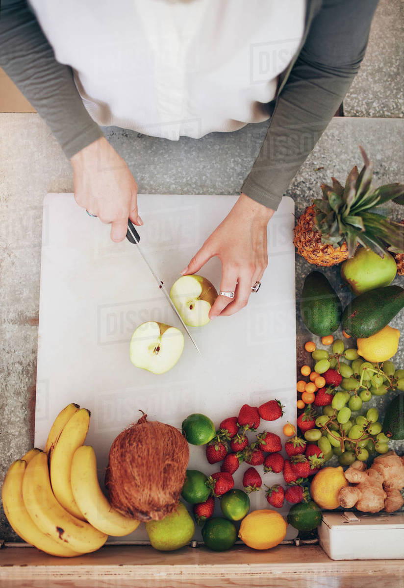 Top view of female employee working at juice bar cutting an apple