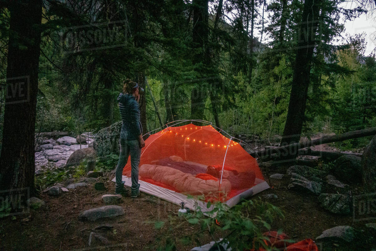 Woman drinking water by tent, camping at night. Stock Photo Dissolve