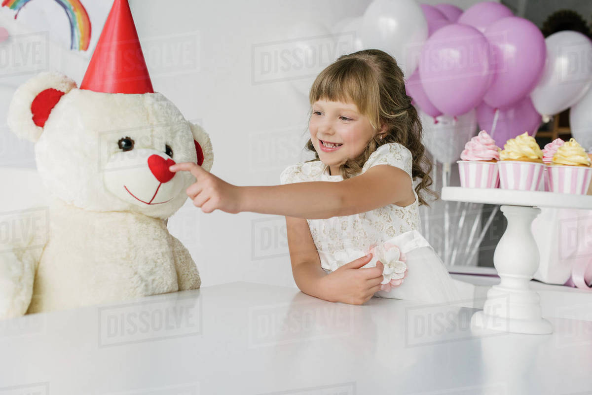 Smiling birthday kid touching nose of teddy bear in cone Stock Photo