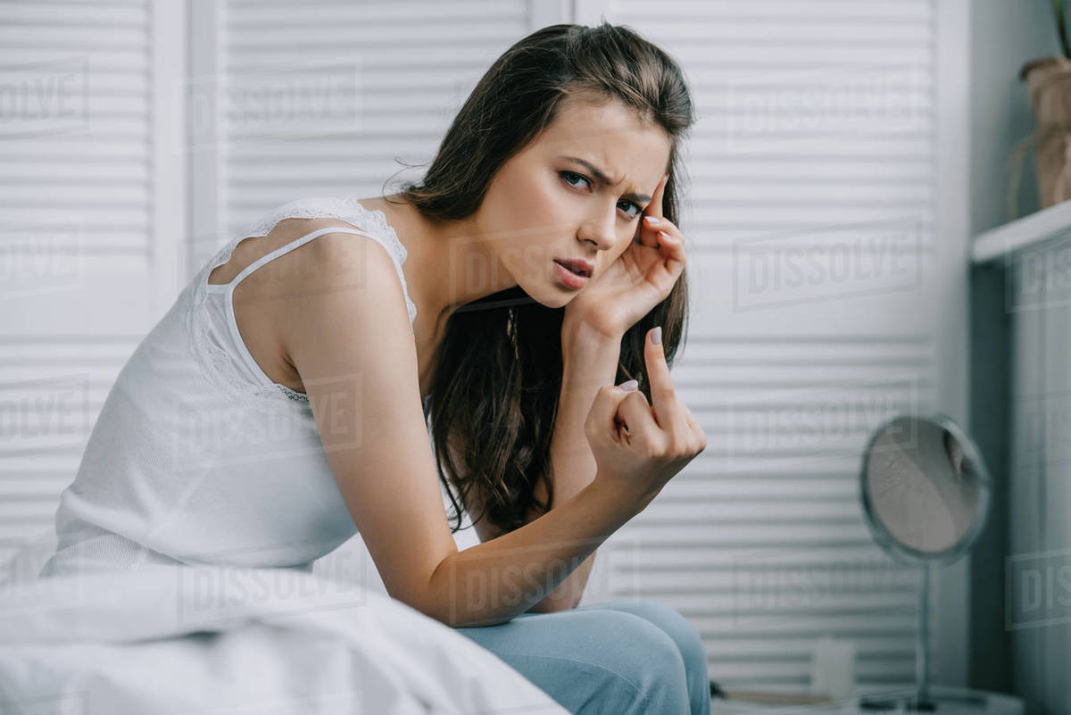 Young woman with headache giving the finger and looking at camera in