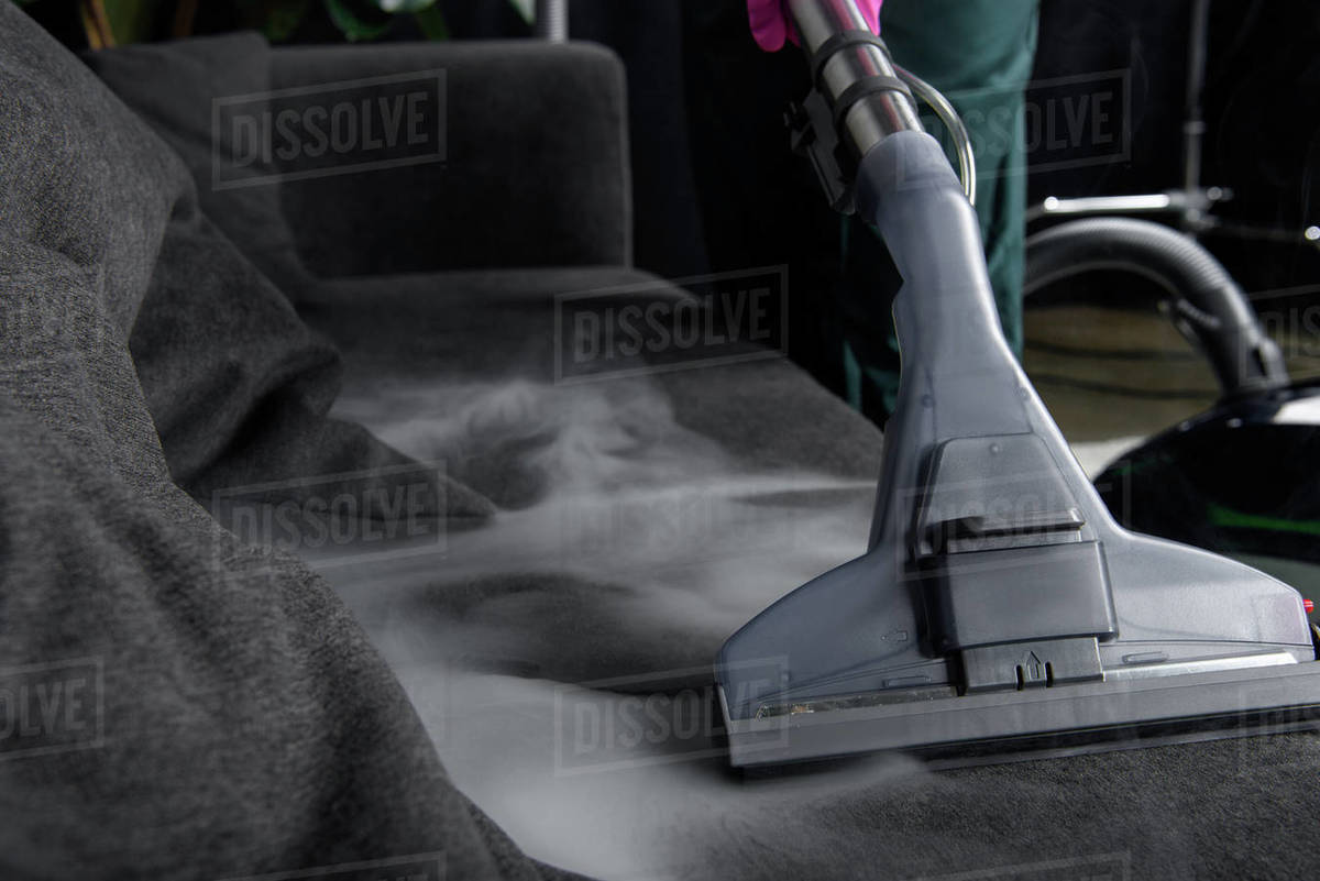 Closeup view of person cleaning sofa with vacuum cleaner, hot steam