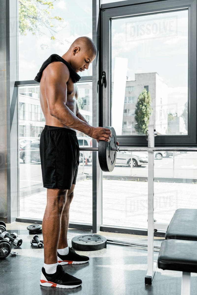 side view of muscular young sportsman with towel putting weight plate