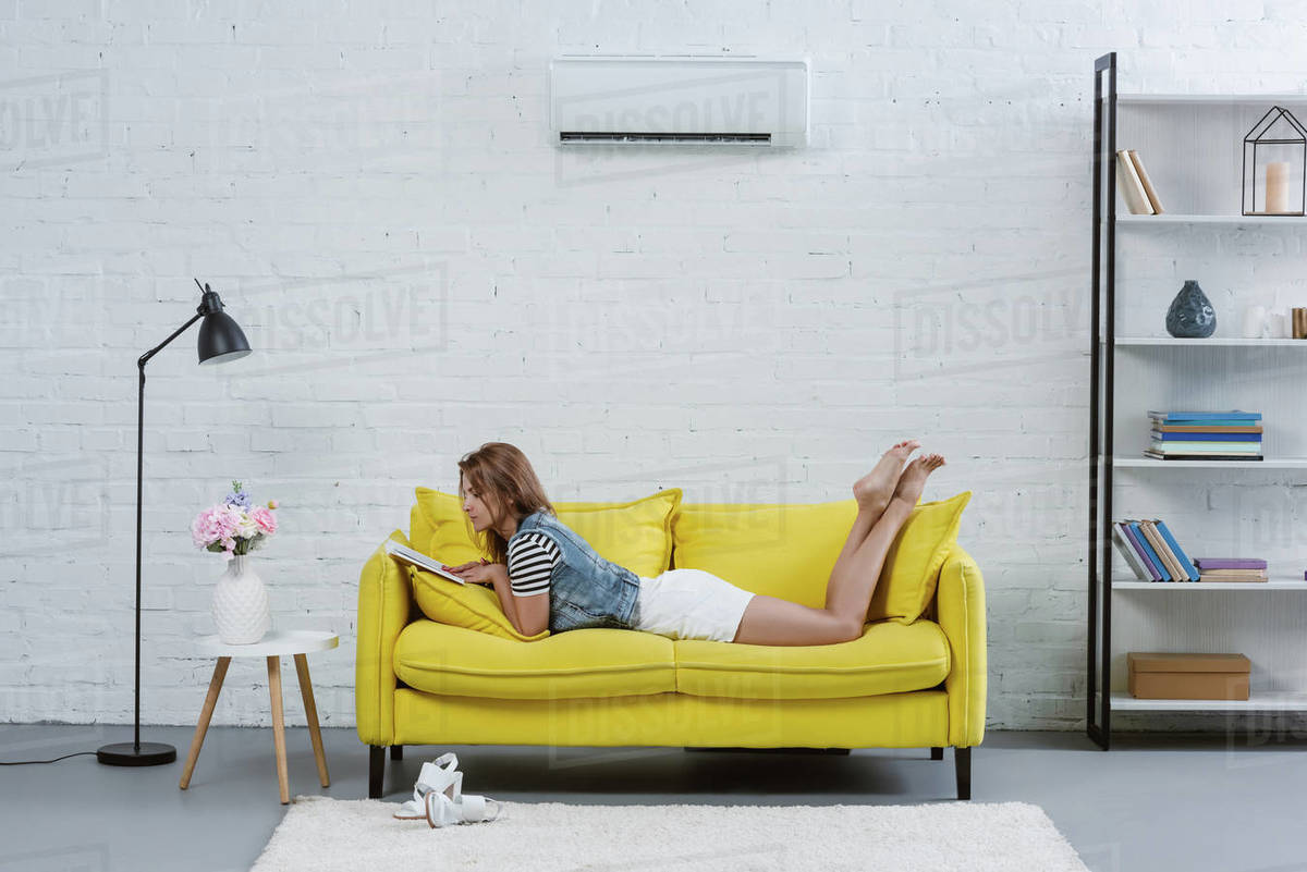 beautiful young woman reading book on sofa under air conditioner