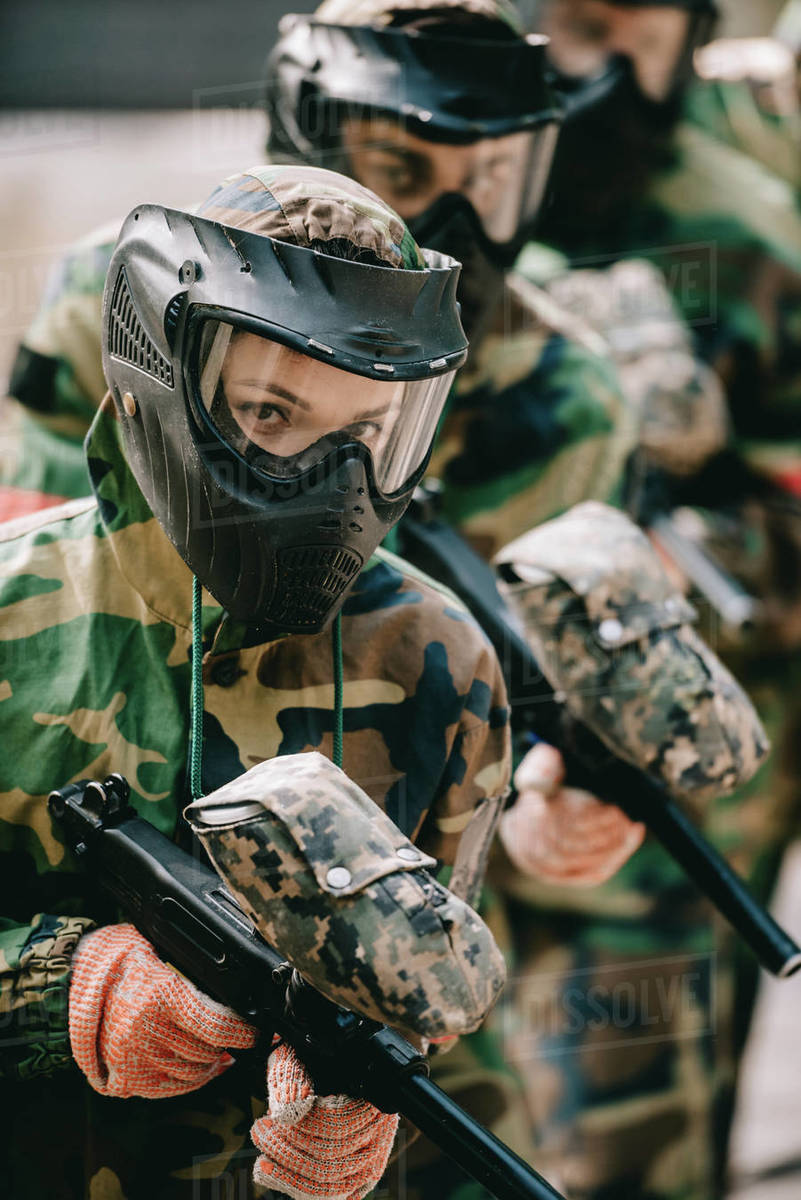 Portrait of female paintball player holding marker gun with her team in