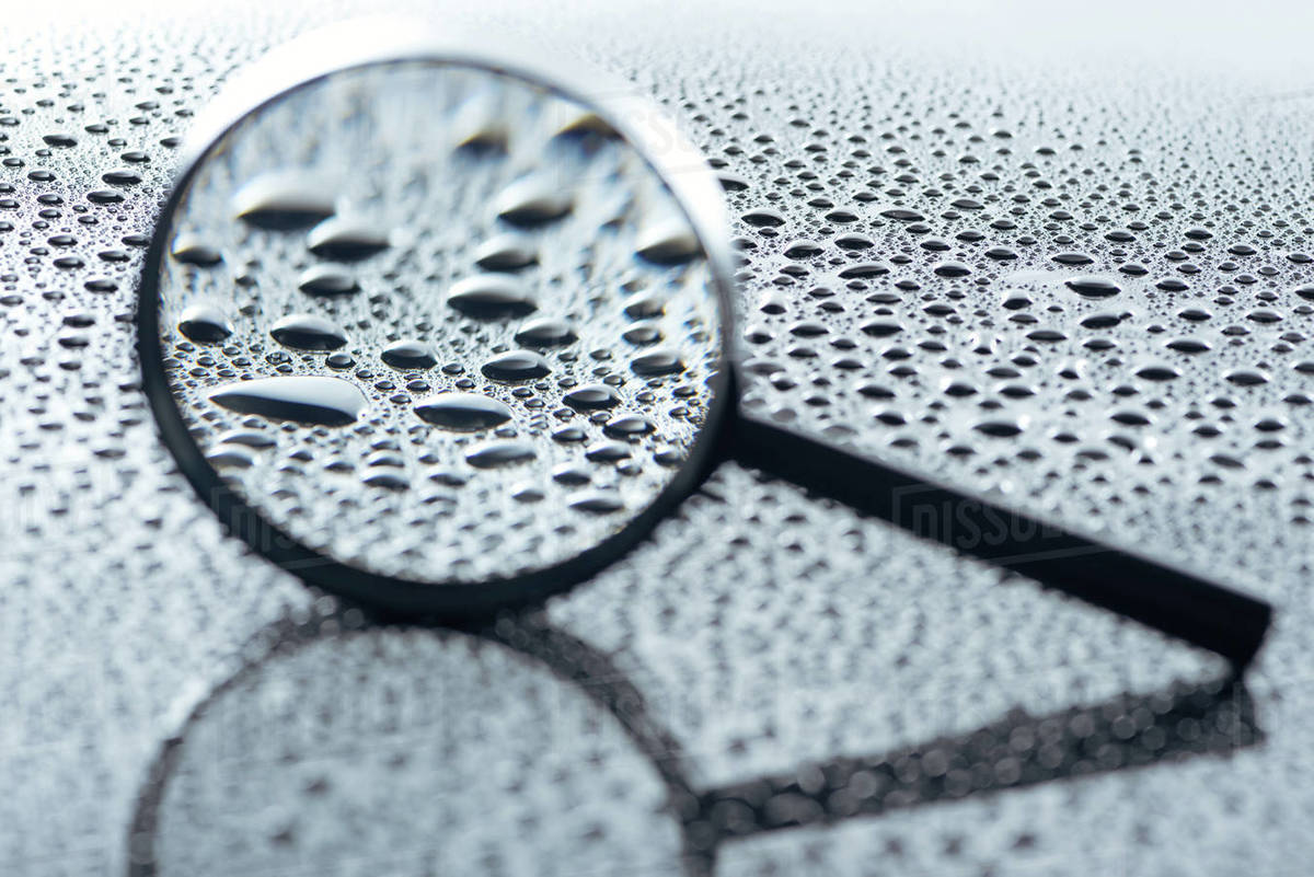 Close up view of magnifying glass and water drops on grey backdrop