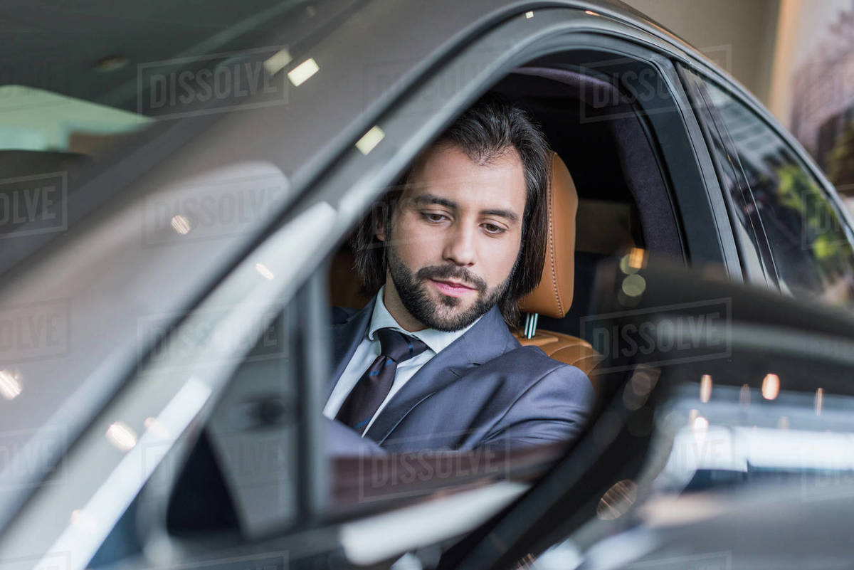 Businessman sitting in new car for test drive in dealership salon