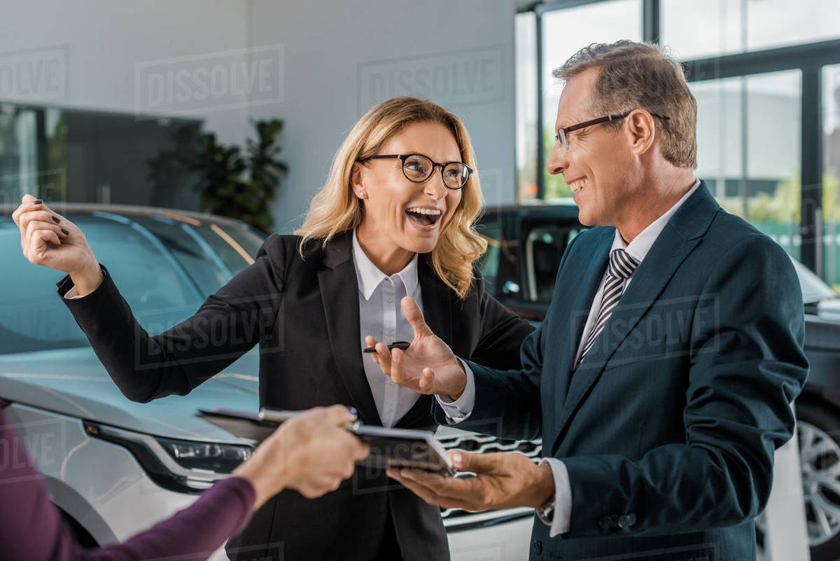 Happy businesspeople and female car dealer with documents in showroom