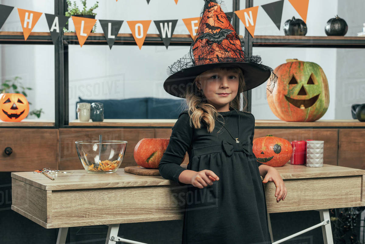portrait of adorable kid in witch halloween costume leaning on wooden